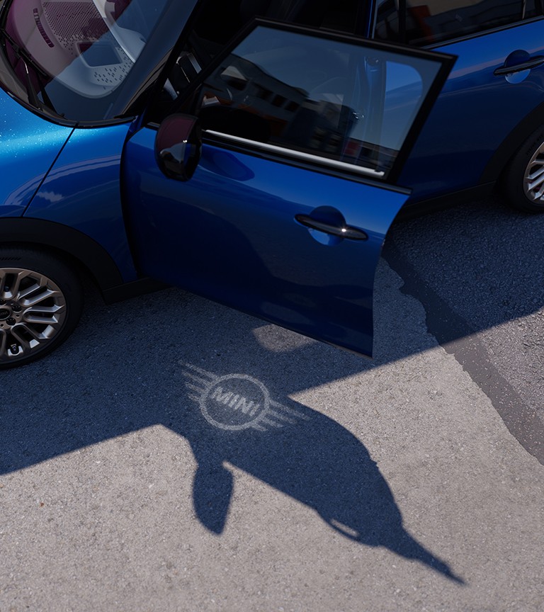 MINI Cooper visto de cima com a porta aberta, estacionado numa rua, com projeção  do logo MINI no chão
